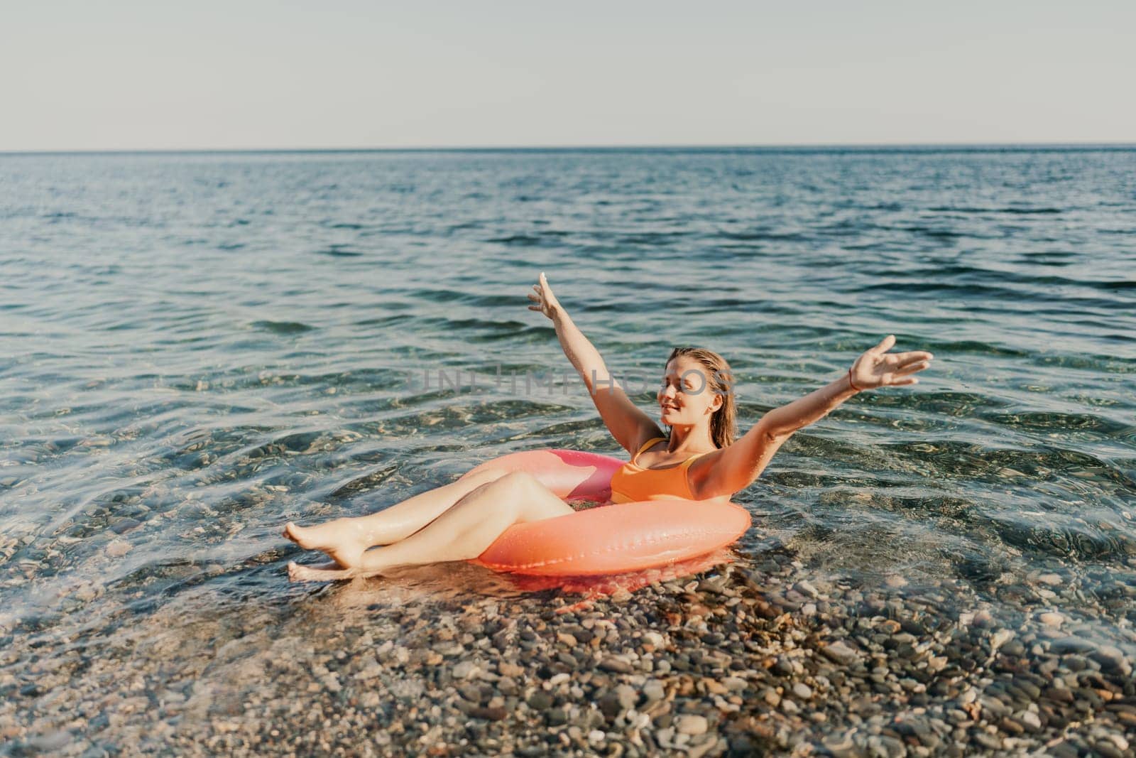 A woman is floating in a red inflatable tube in the ocean. She is smiling and she is enjoying herself