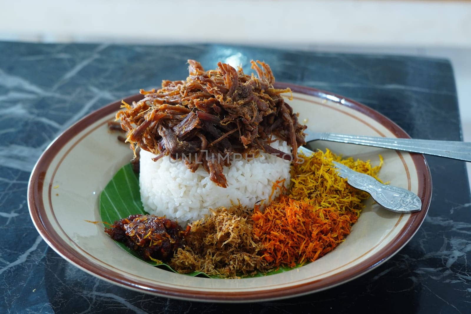 Nasi Krawu, a signature dish from Surabaya, Indonesia, featuring savory shredded beef, fragrant rice wrapped in a banana leaf, and an array of vibrant condiments - sambal, fried shallots, and turmeric.