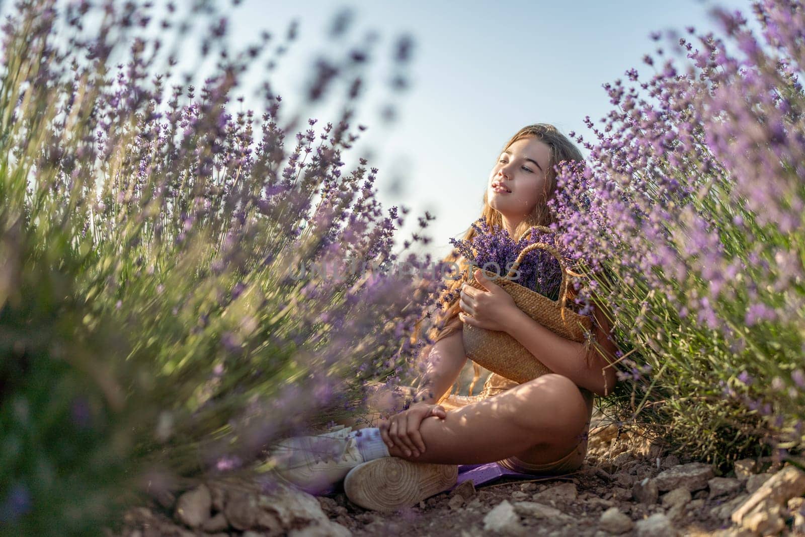 Girl is sitting in a field of purple flowers. She is holding a basket of flowers and smiling. Scene is peaceful and serene, as the girl is surrounded by the beauty of nature