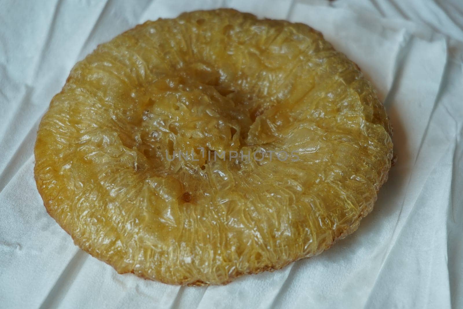 A crispy, golden-brown kue cucur, a traditional Indonesian snack made from rice flour and coconut milk, resting on a white paper napkin