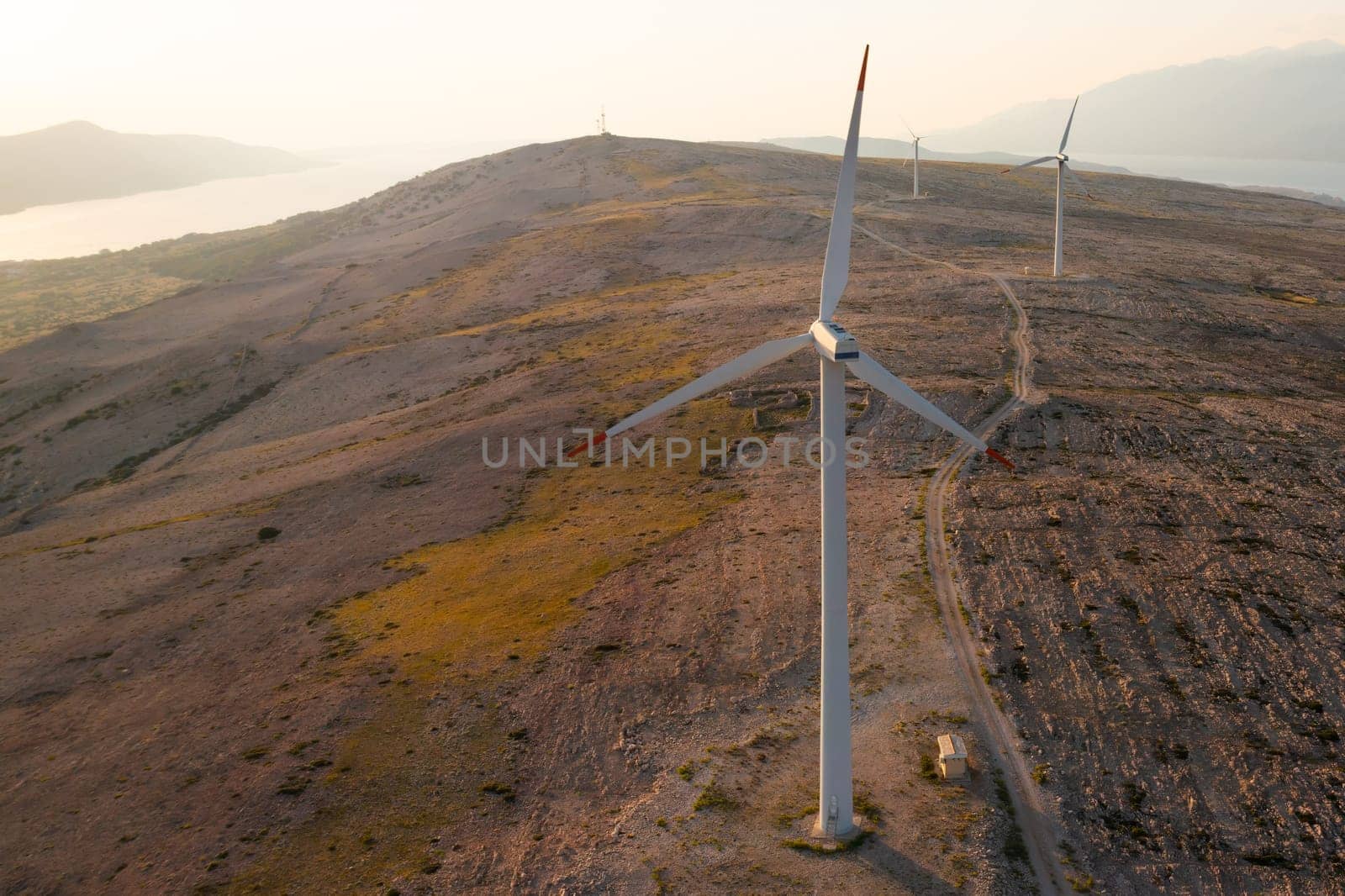 Blades of wind turbines rotate generating power on Pag Island at sunset twilight. Eco-friendly solution to convert wind into power on hill in Croatia
