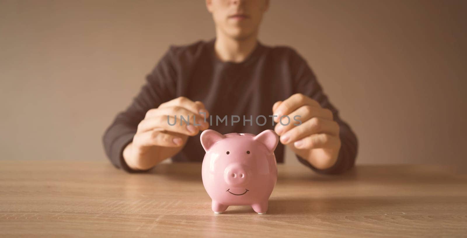A young man is sitting at his workplace, in the foreground is a piggy bank. A businessman saves his money, takes care of the safety of his earnings, develops his business and makes investments.