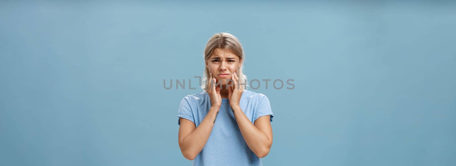 Girl feeling pain in teeth after drinking hot coffee. Displeased unhappy troubled young girl with blond hair frowning feeling discomfort in mouth holding hands on cheeks suffering toothache.