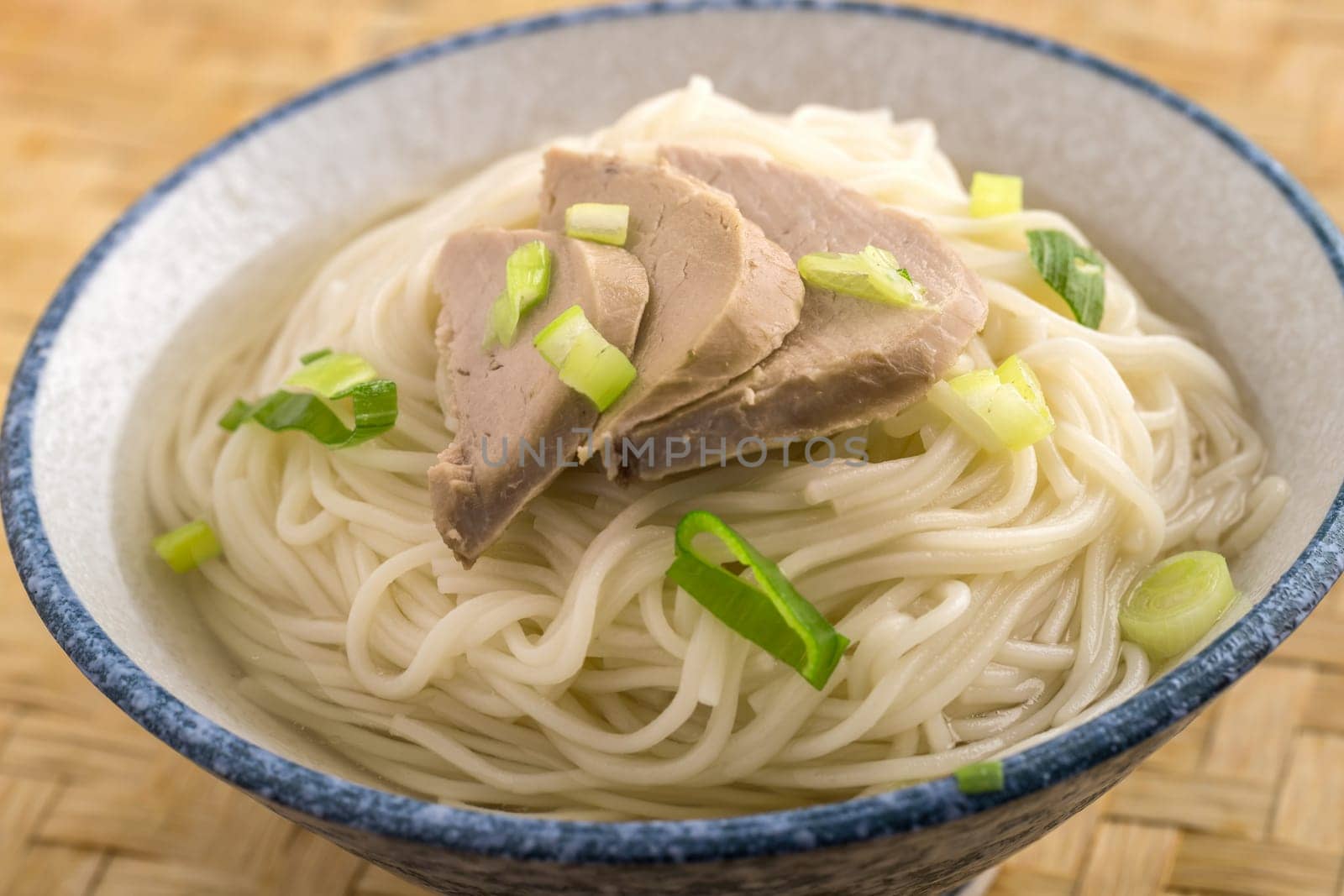 A close up of a bowl of noodles topped with pork slices and green onions.