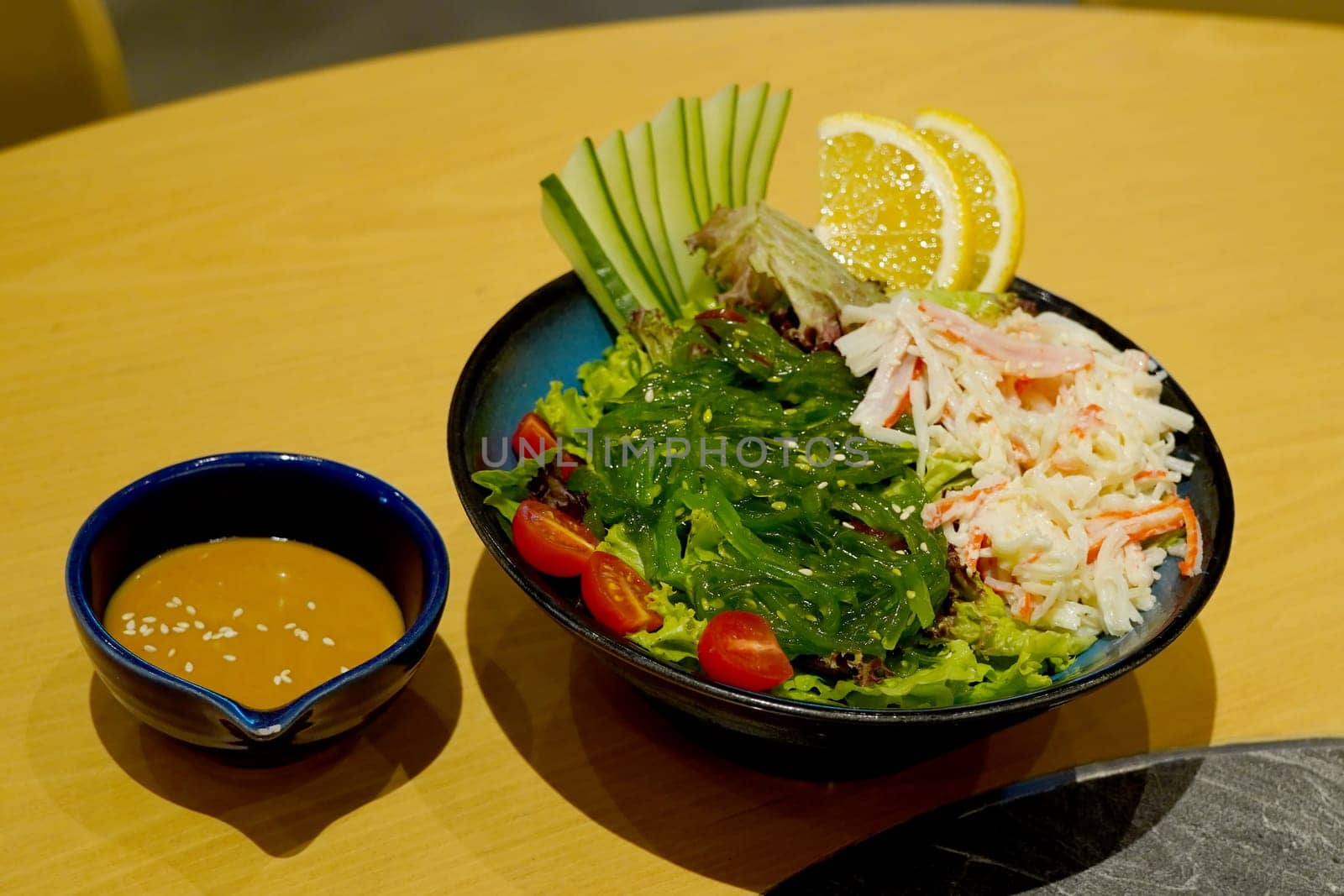 A vibrant Japanese salad featuring seaweed, crab meat, lettuce, tomatoes, cucumbers, and orange slices, served with a creamy sesame sauce.