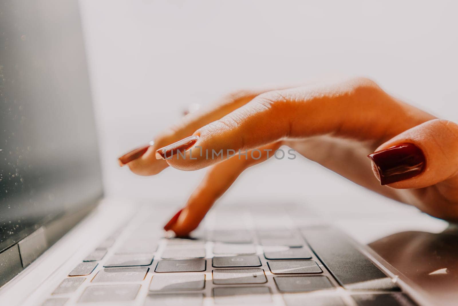 A hand with red nail polish types on a laptop keyboard.