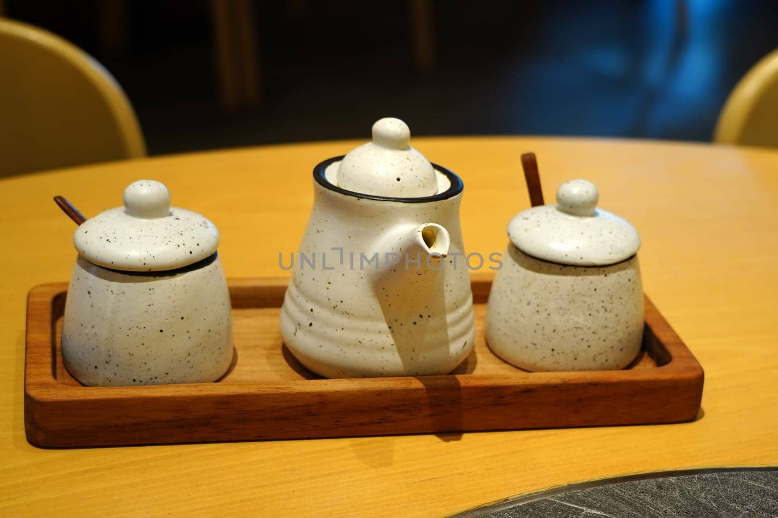 A set of Japanese pottery consisting of a small teapot and two lidded jars, arranged on a wooden tray against a dark background. The pottery is white with speckles and has a rustic, handmade feel.