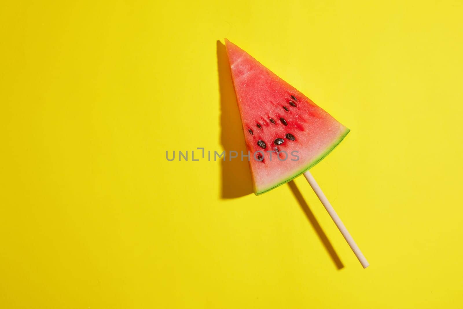 triangle piece of watermelon on stick on yellow background, summer concept