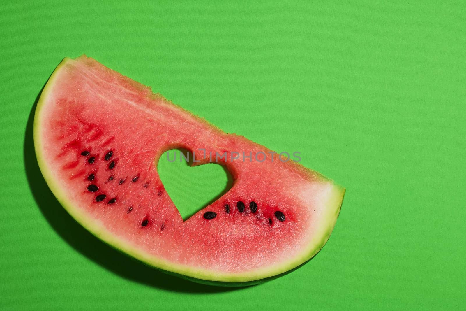 Ripe watermelon slice with heart shaped hole on green background, summer concept