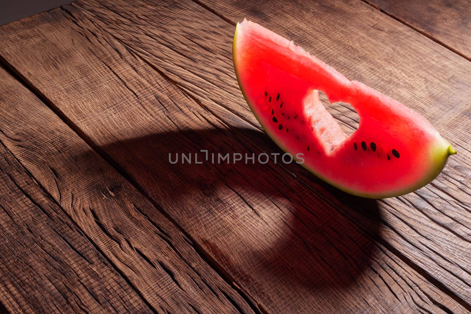 Ripe watermelon slice with heart shaped hole on blue background of the blue sky with little cloud on a hot summer day