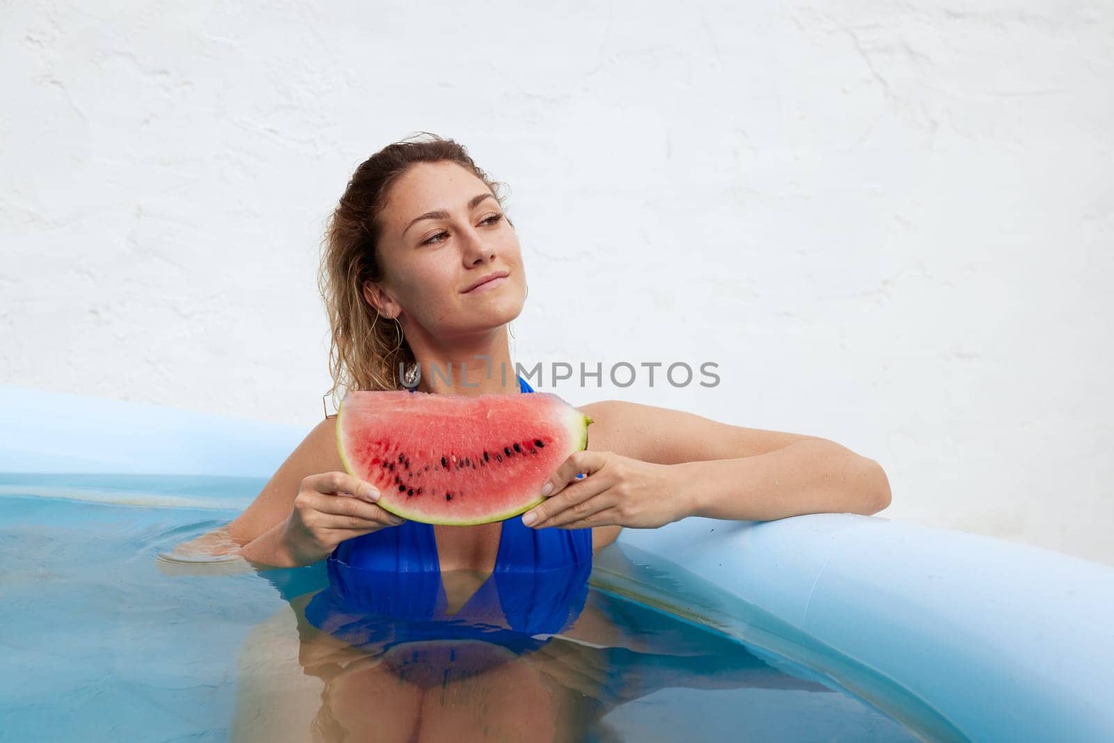 a girl in a bathing suit swims in the pool in a hot summer, a girl with a watermelon, summer holiday concept