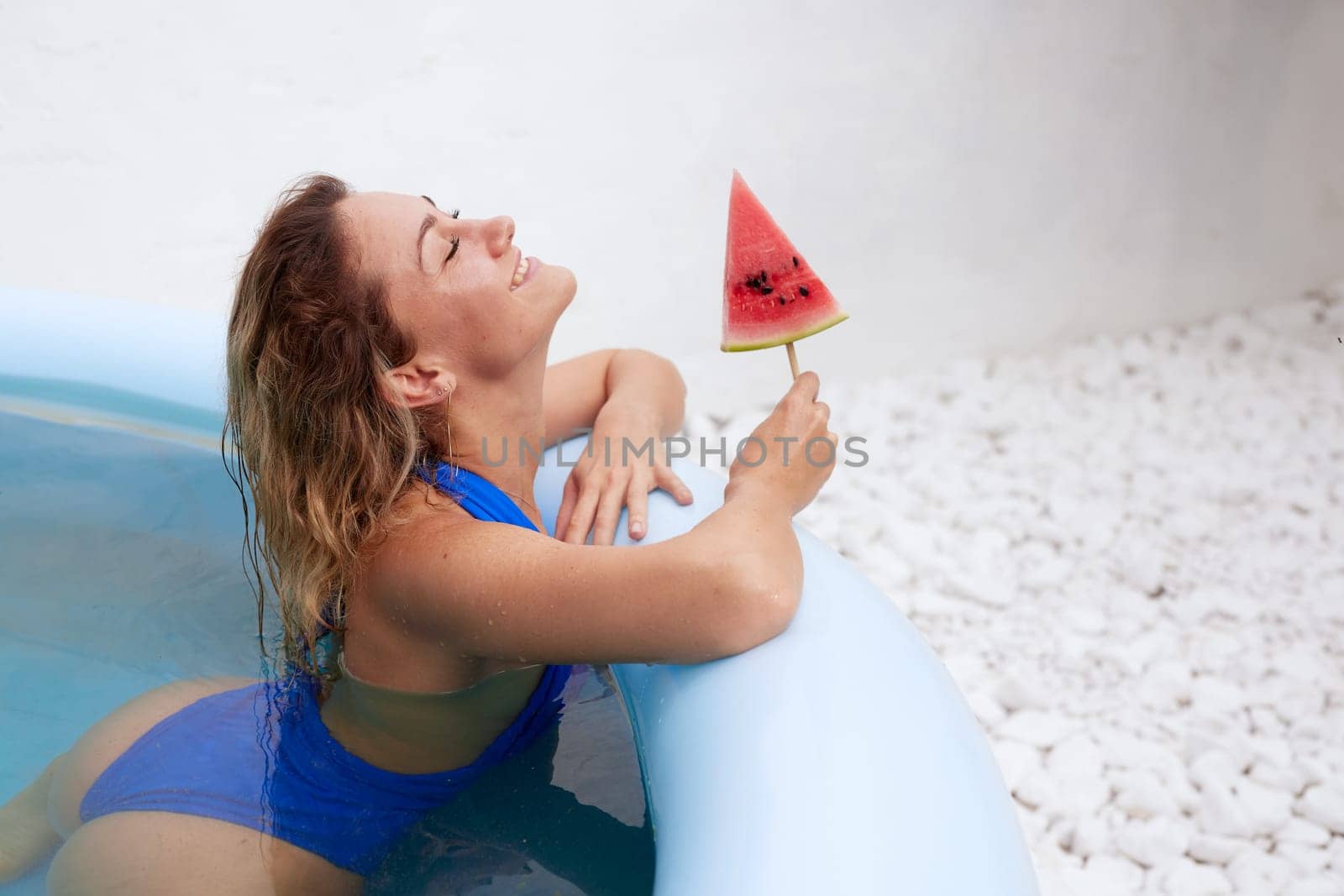 a girl in a bathing suit swims in the pool in a hot summer, a girl with a watermelon, summer holiday concept