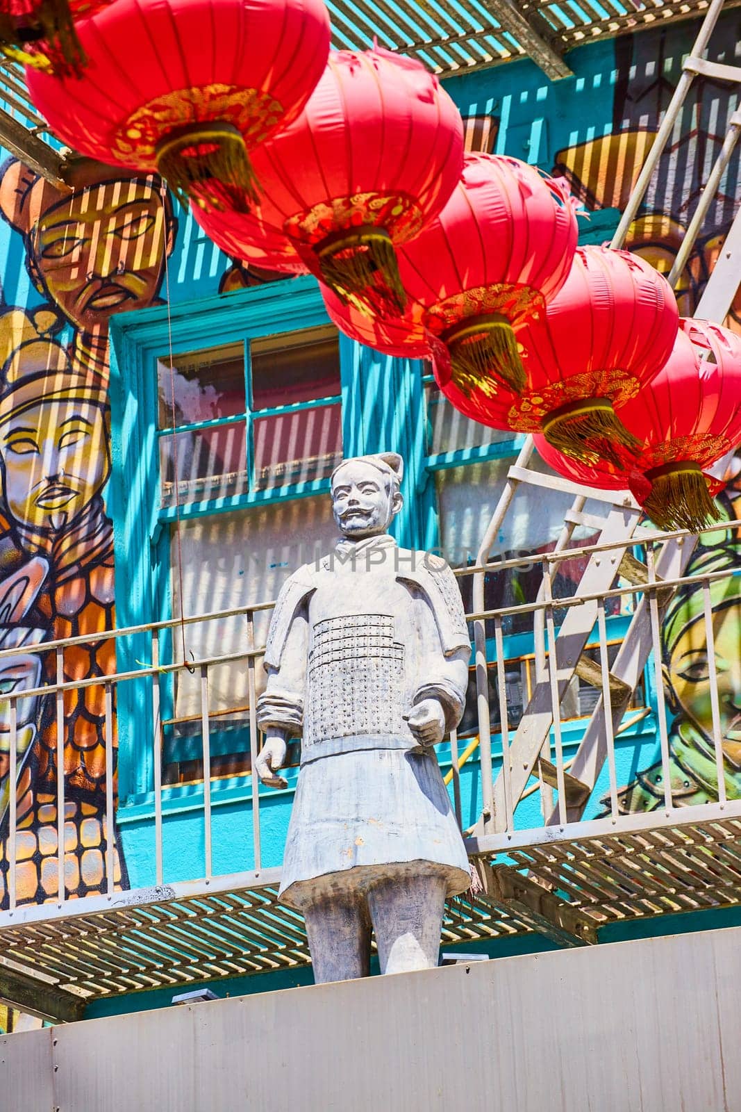 Image of Soldier statue of man standing in front of blue windows and painted mural with hanging red lanterns