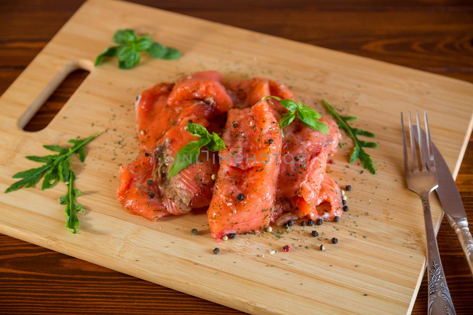Fresh big pieces of salted red fish with spices and herbs on a wooden board.