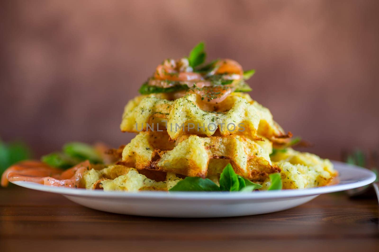 Cooked potato waffles with lightly salted red fish and herbs in a plate, on a wooden table.
