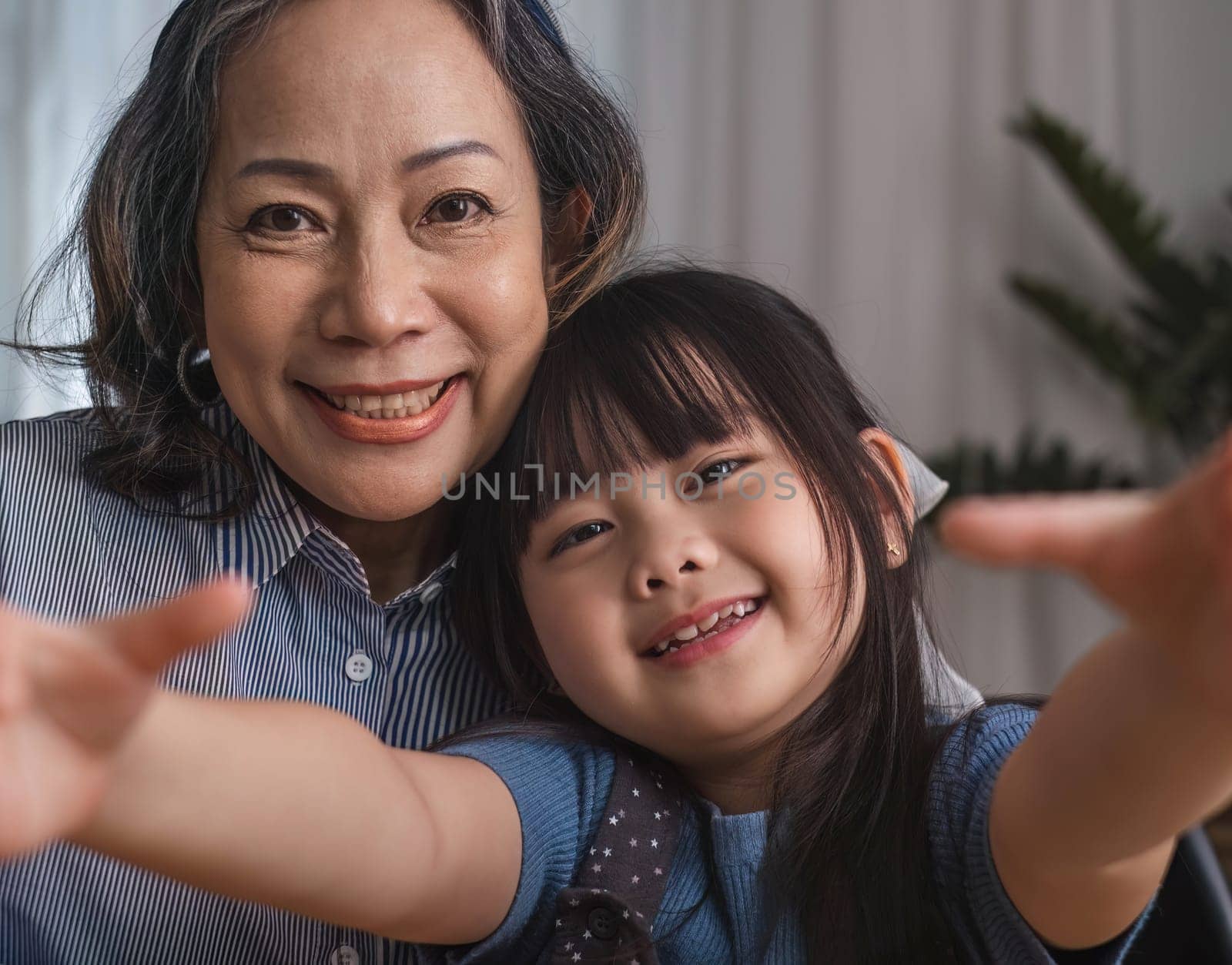 Grandma and granddaughter happily sit and play together in the living room. by wichayada