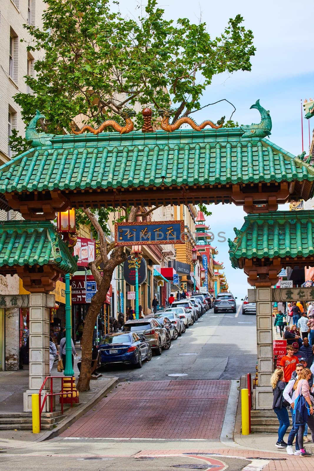 Image of Pedestrians and cars around iconic San Francisco Chinatown entrance with green tree behind it