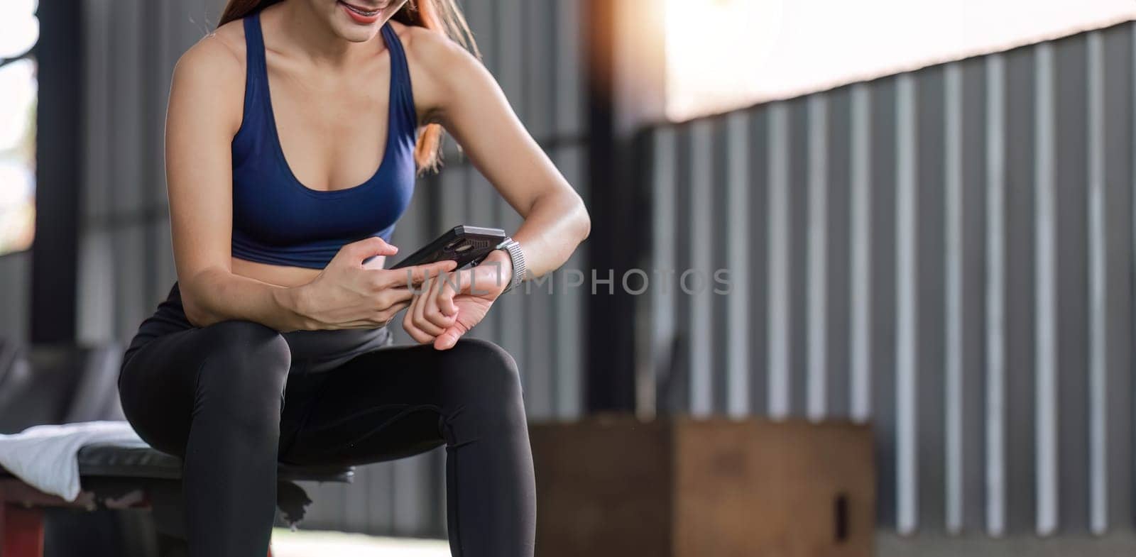 Young female athlete in sportswear sits at the gym using a cell phone while relaxing..