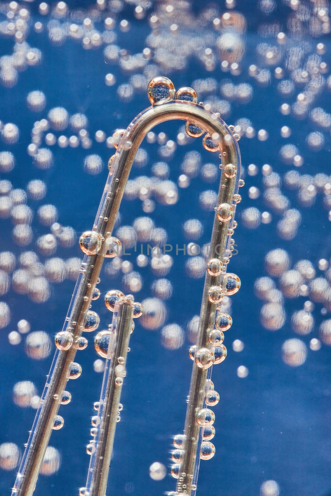 Image of Macro of silvery bubbles on paperclip with bubbly blue background