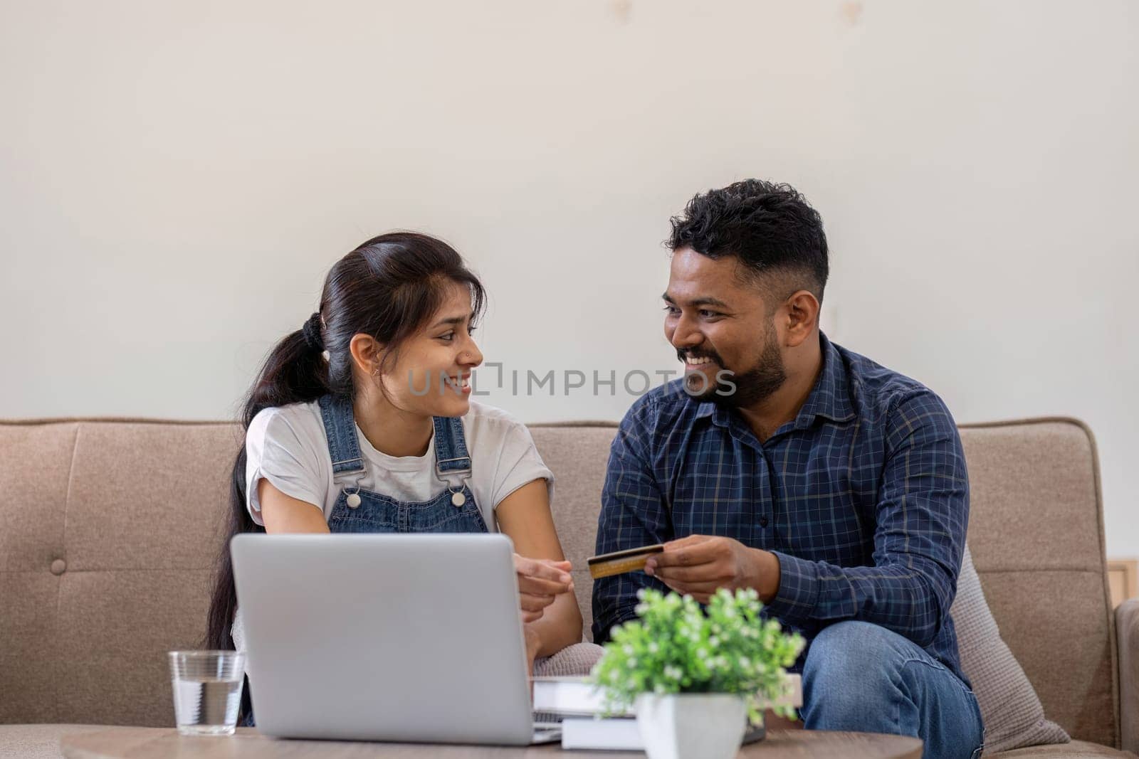 Happy couple using credit card to make online purchases on laptop in living room. by wichayada