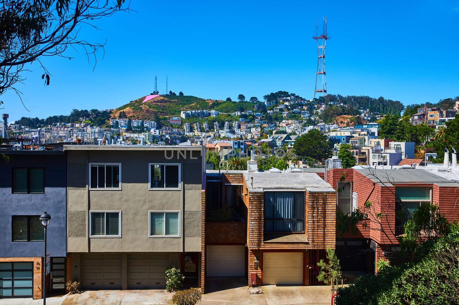 Image of Sutro Tower up on hill on blue sky day with houses down below on hillside