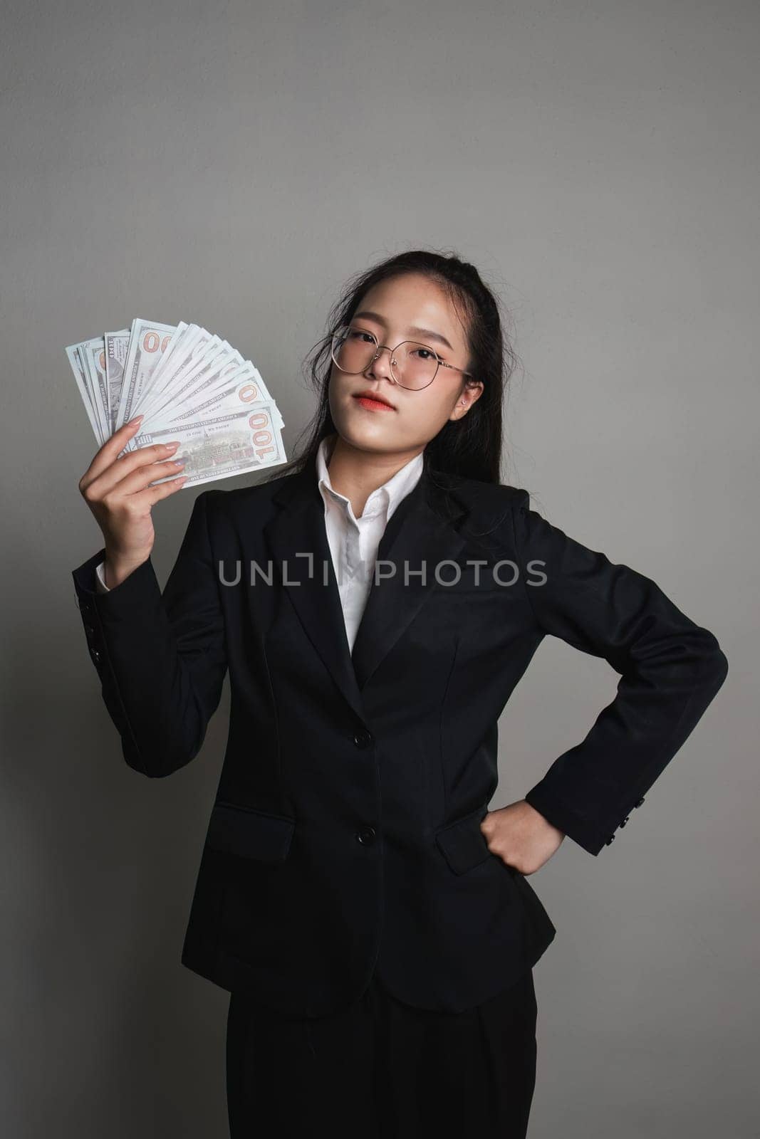 Young Asian woman holding a dollar bill in her hand standing on a gray background..
