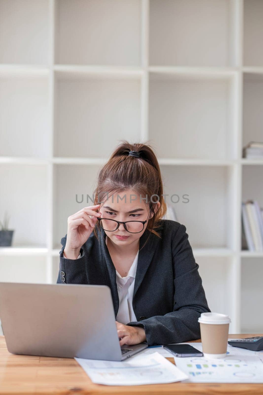 Confused Asian woman thinking hard about how to solve problems online looking at laptop screen. Serious Asian businesswoman worried focused on solving difficult computer at office by wichayada