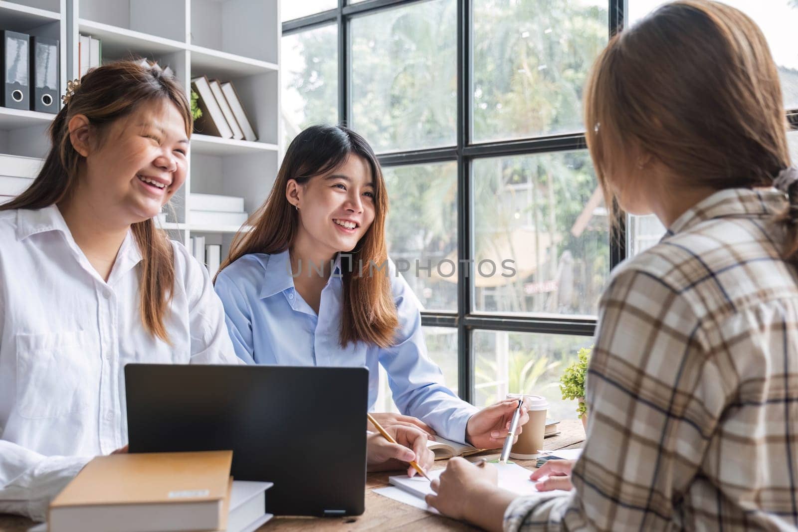 Asian College groups of students using laptop, tablet, studying together with notebooks documents paper for report near windows in classroom. Happy young study for school assignment, Soft focus by wichayada