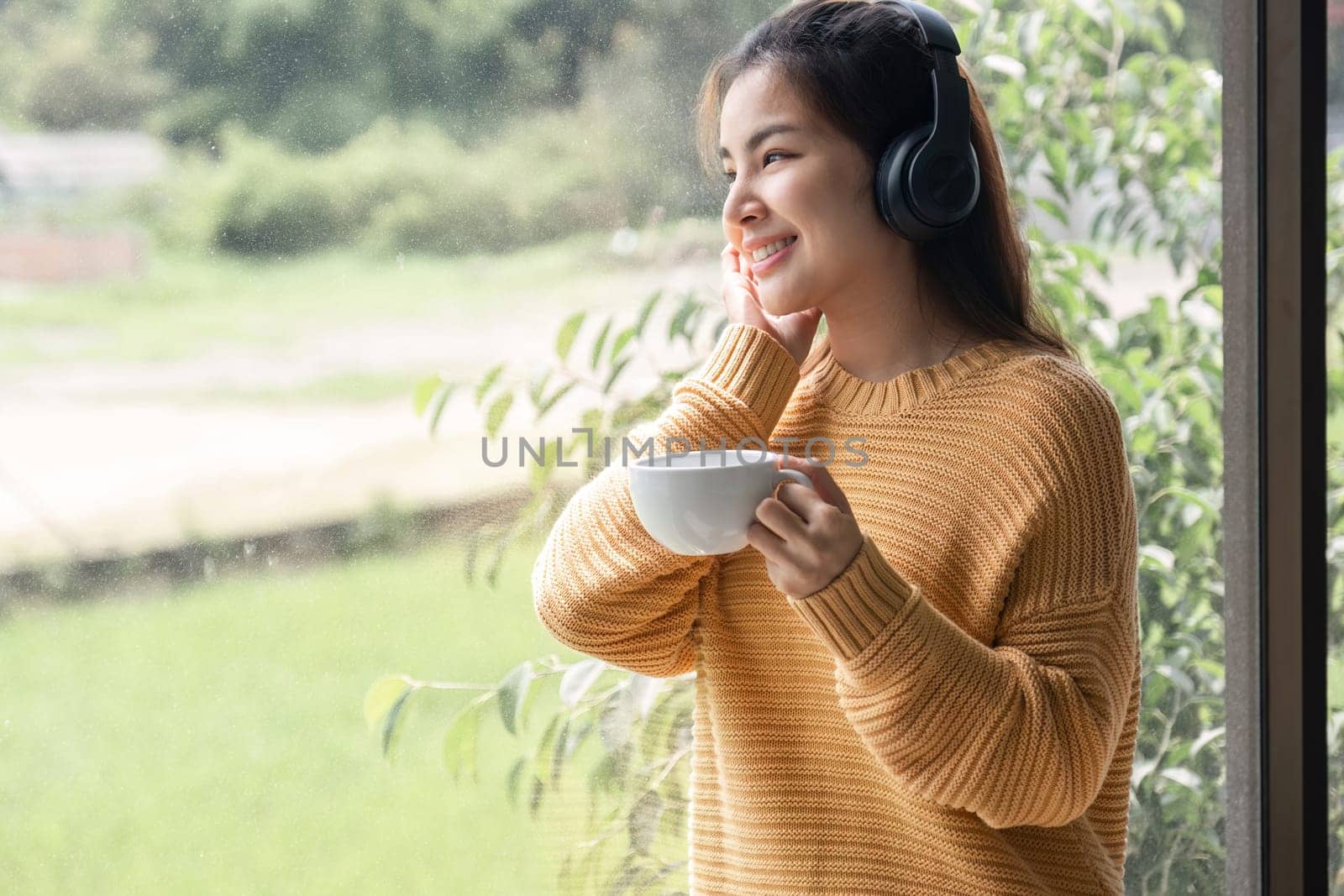 Portrait of beautiful young woman with a cup of coffee and wearing headphones standing relaxed and happy..