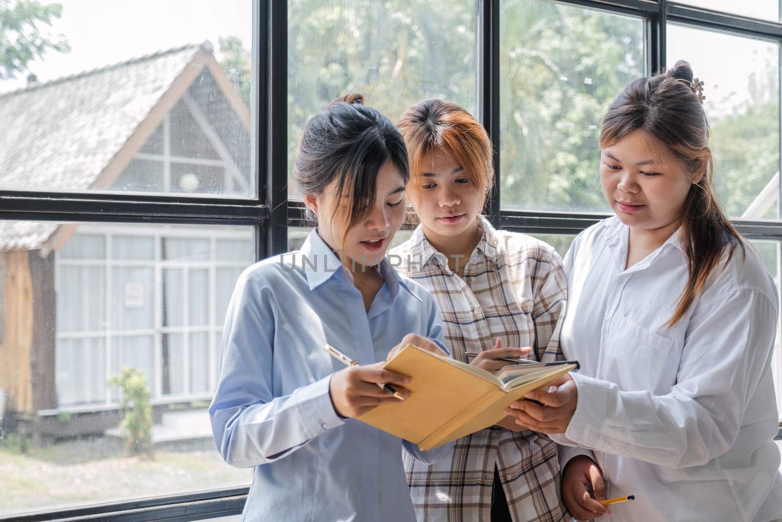 Asian College groups of students using laptop, tablet, studying together with notebooks documents paper for report near windows in classroom. Happy young study for school assignment, Soft focus by wichayada