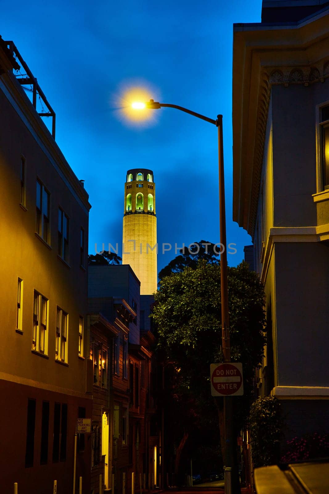 Image of Gorgeously illuminated Coit Tower at night seen from darkly lit ally street