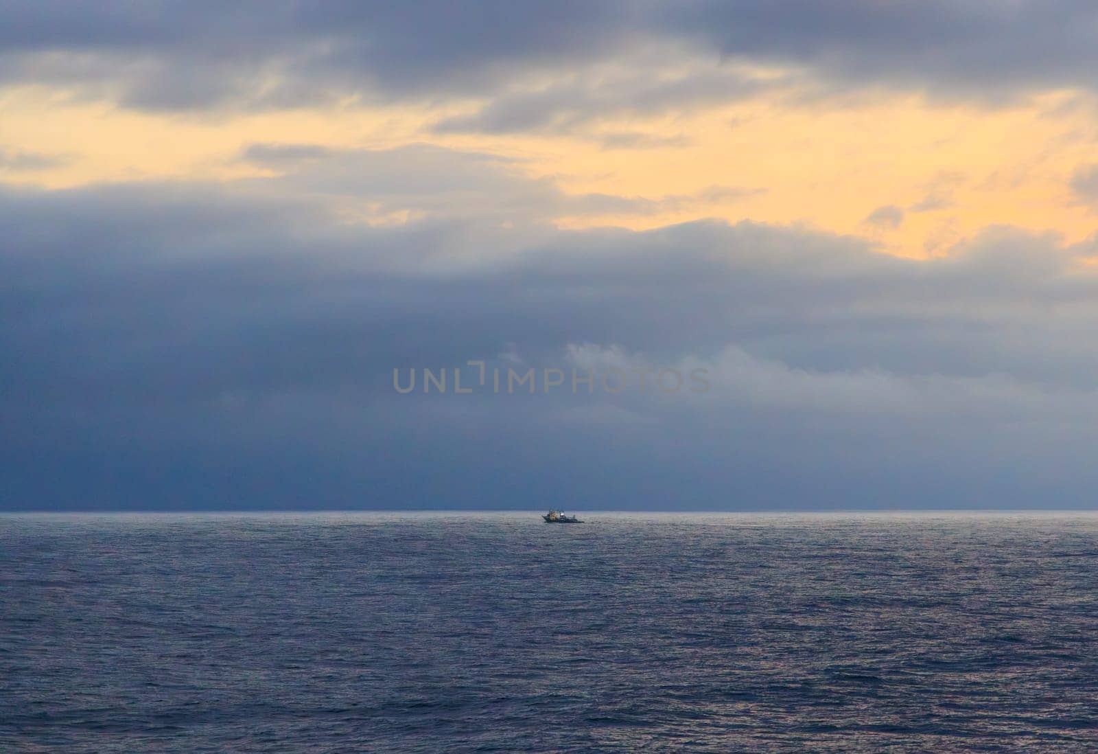 Storm approaches distant fishing boat on horizon at sunrise. High quality photo