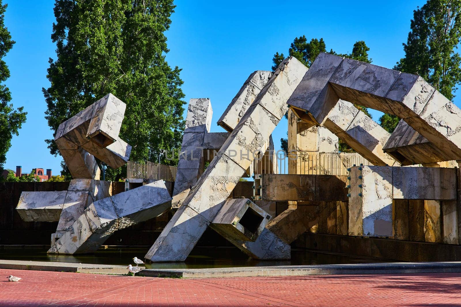 Image of Abstract concrete cubed sculpture in tiny pond with seagulls on red brick sidewalk