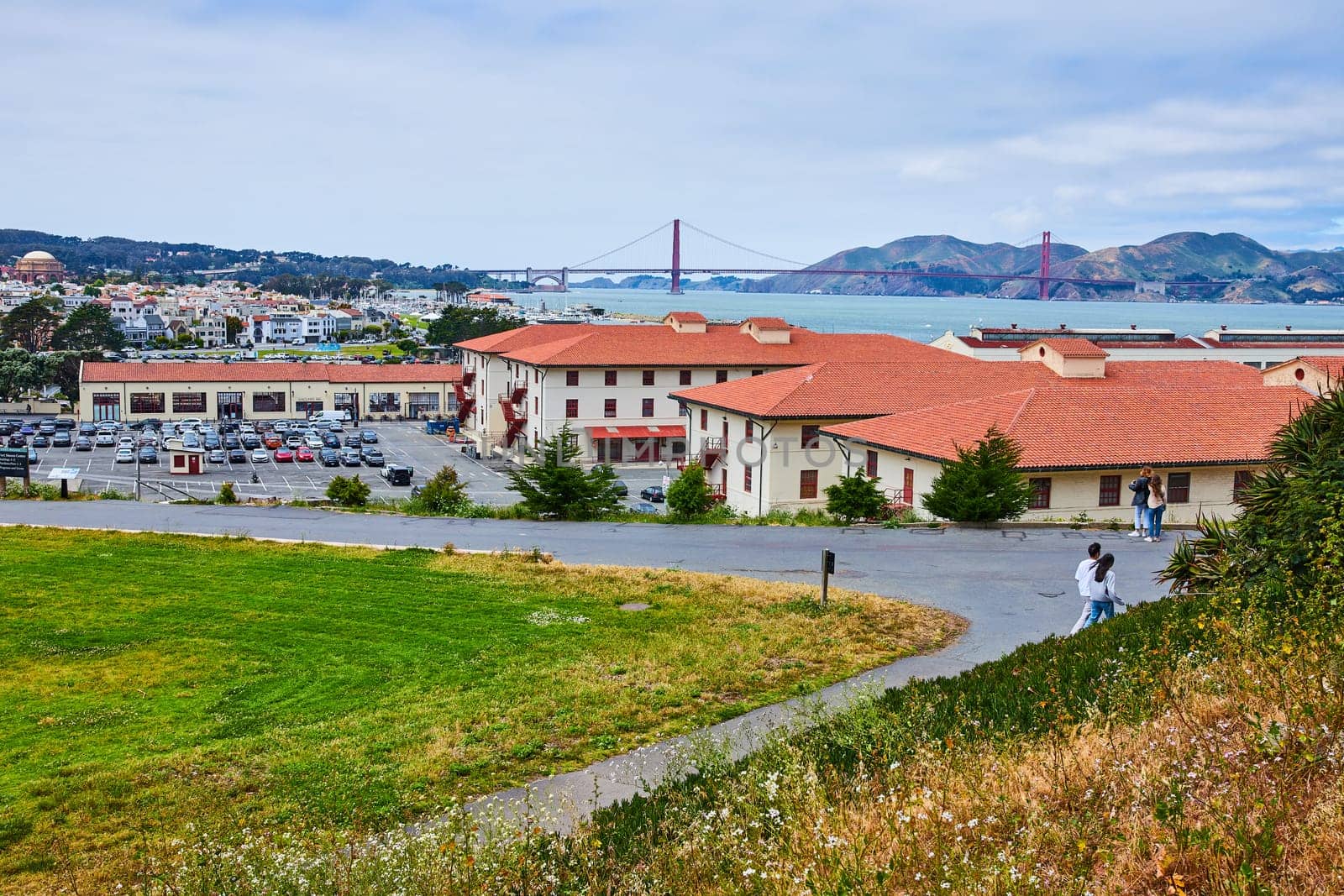 Image of Orange shingle roofs buildings and people walking on path toward San Francisco Bay with bridge