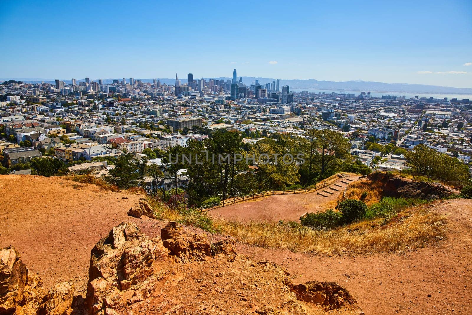 Image of Dirt park trail winding down hillside to San Francisco city and downtown with distant bay waters