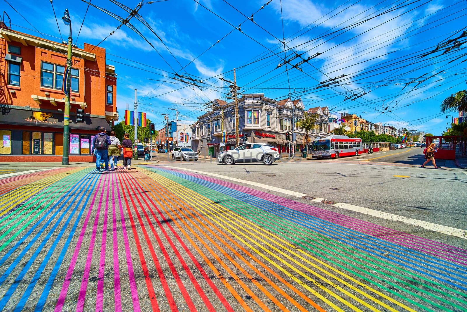 Image of People crossing rainbow crosswalk with brilliant blue sky overhead in Castro District