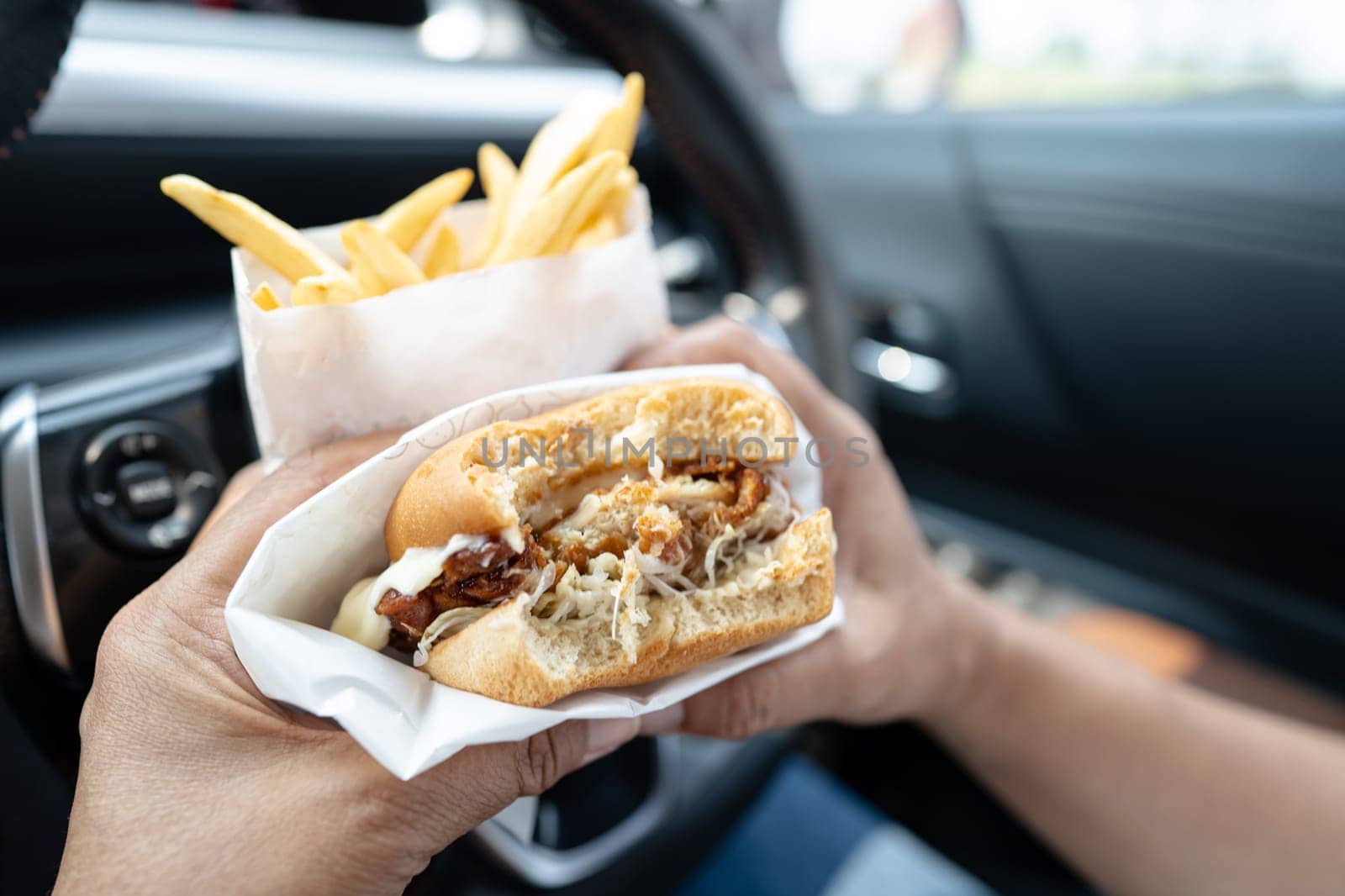 Asian lady holding hamburger and French fries to eat in car, dangerous and risk an accident.