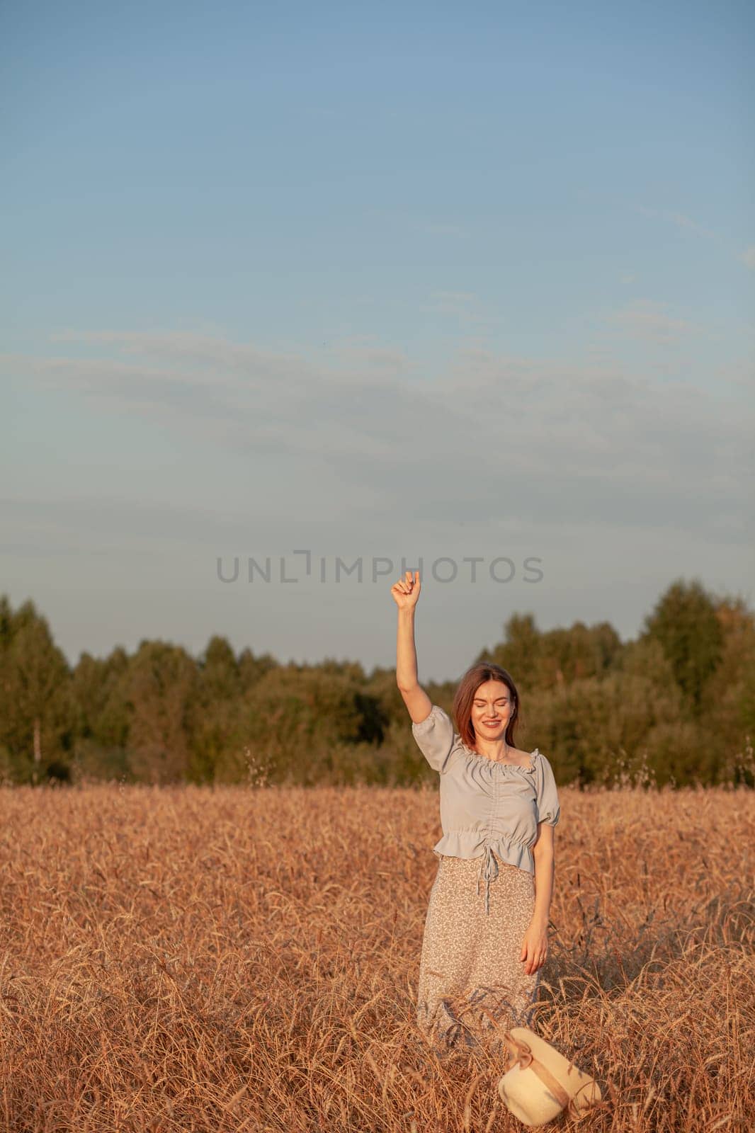 A girl holds a hat in her hand against the background of a wheat field by AnatoliiFoto