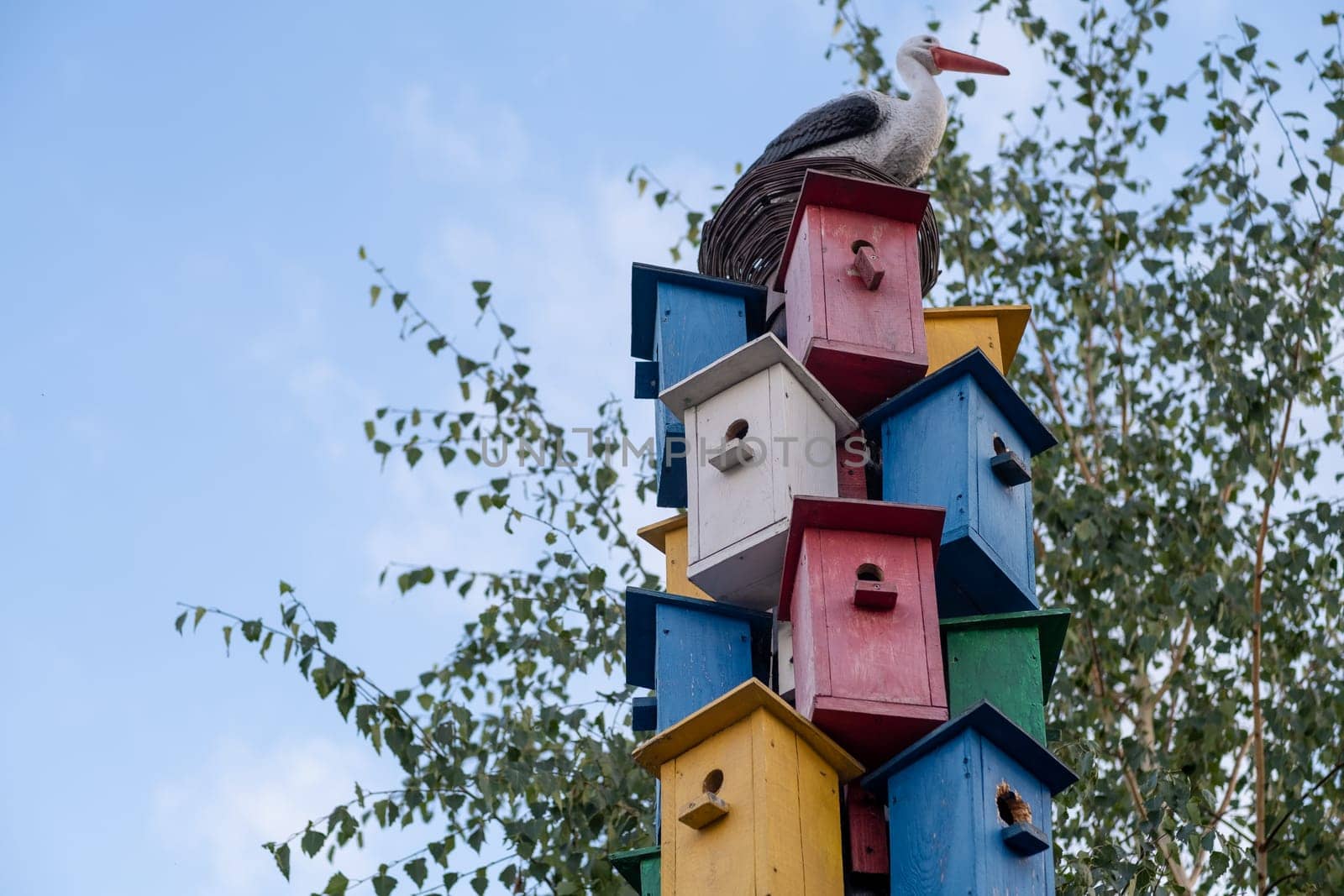 Many different forms of bird feeders. Birdhouses hang on a fence. Bird feeders in the park. Beautiful designer birdhouses for feeding birds. A lot of nesting boxes or houses for feeding the birds.