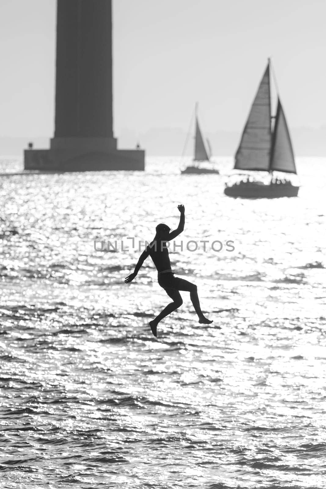 Teenage boy jumping in the water from a pier - black and white image by Studia72
