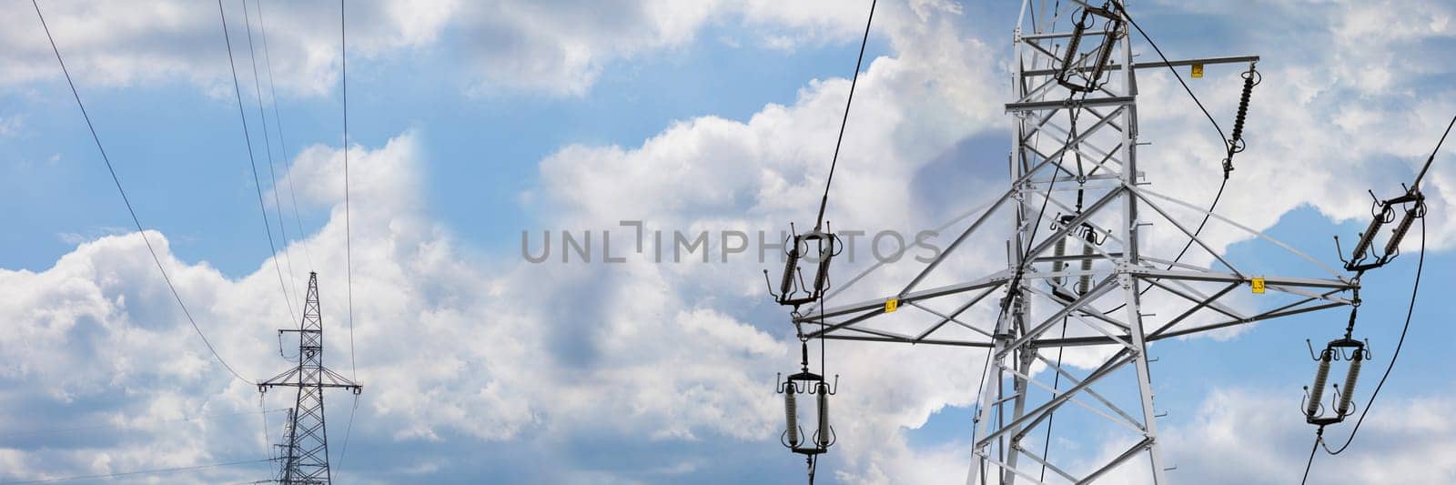 The sky strewn with white clouds in a shot of a narrow panoramic frame with high voltage line poles on it. Energy management.