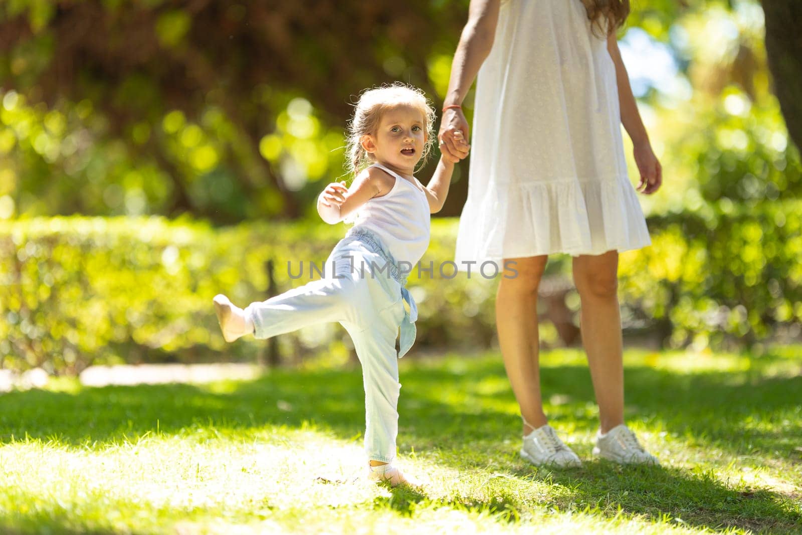 A little girl walking in the park holding her mother by hand. Mid shot