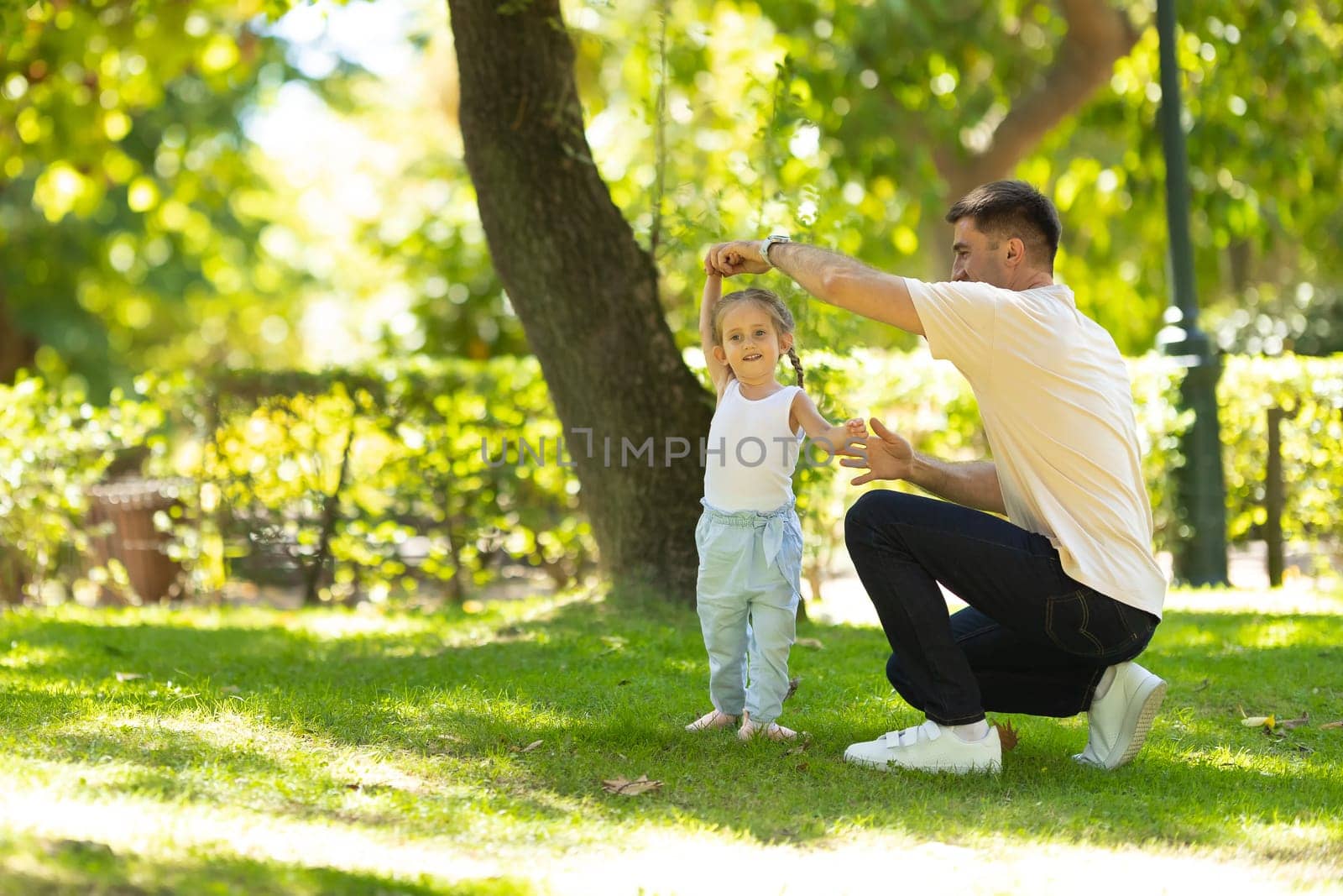 A little girl walking in the park holding her father by hand. Mid shot