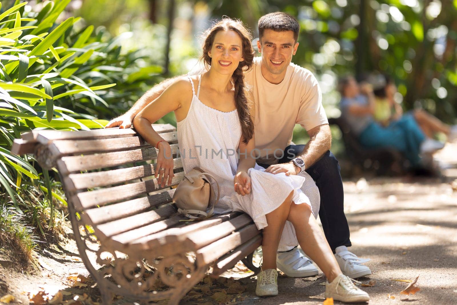 Smiling happy parents sitting on a bench in the park. Mid shot