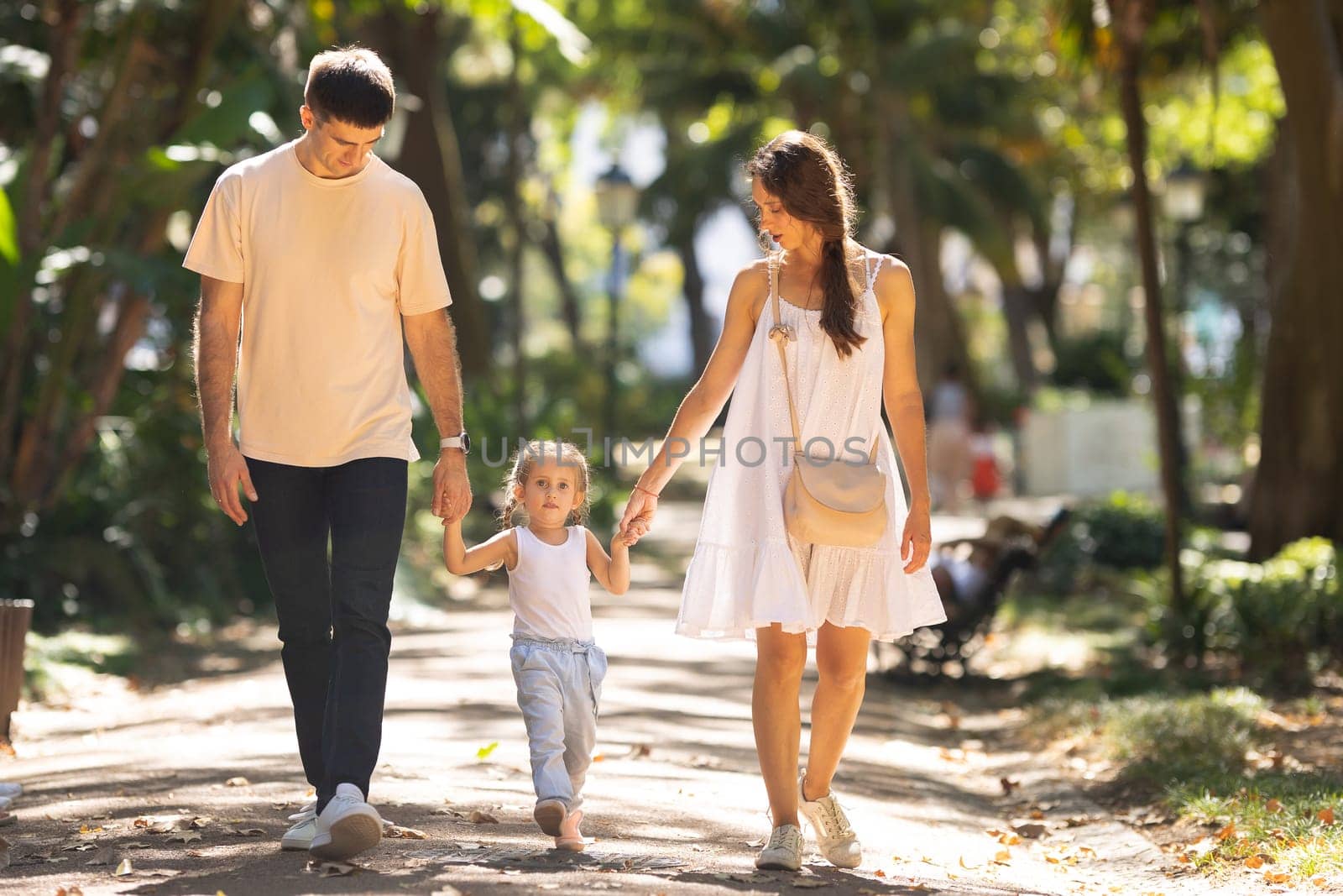 Young family walking in a summer park holding hands. Mid shot