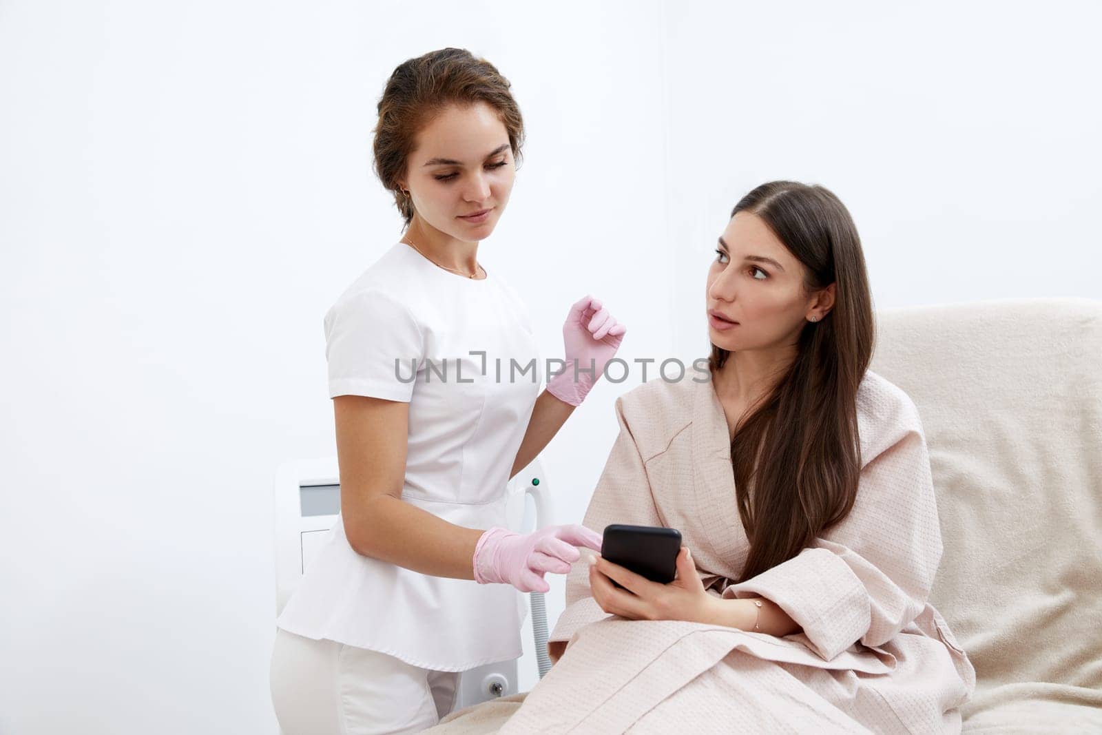 Young female cosmetologist and patient engage in beauty procedure discussion by Mariakray