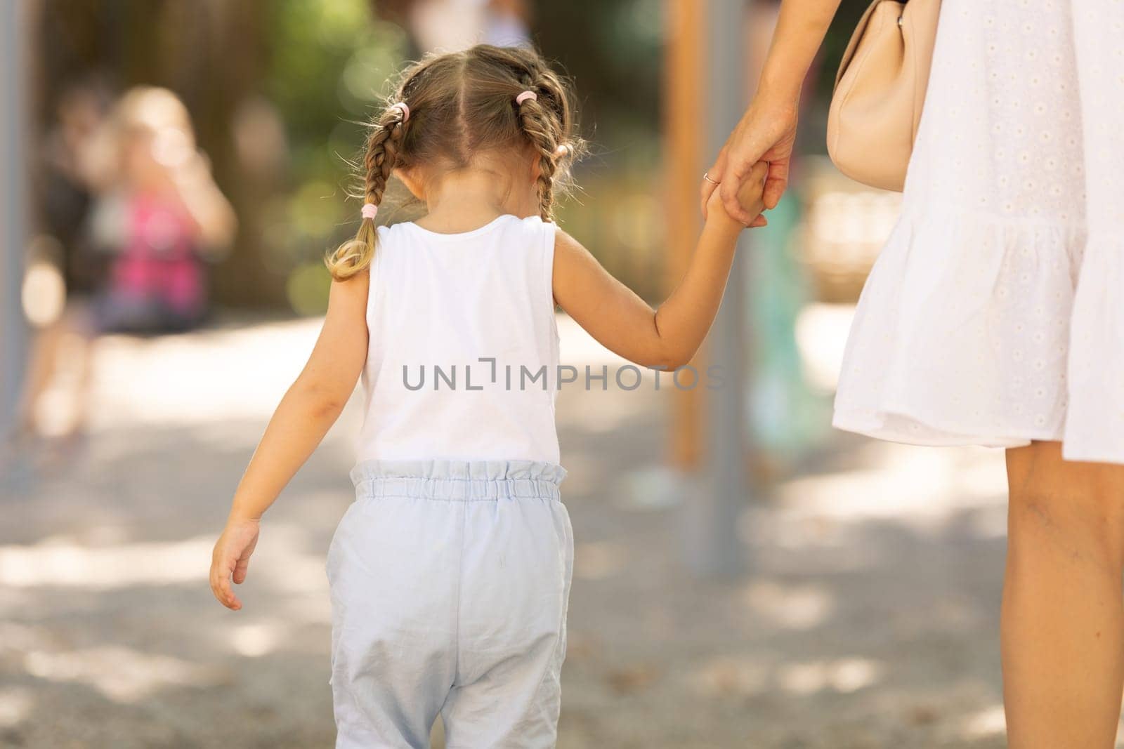 A little girl walking in the park holding her mother by hand - view from the back. Mid shot