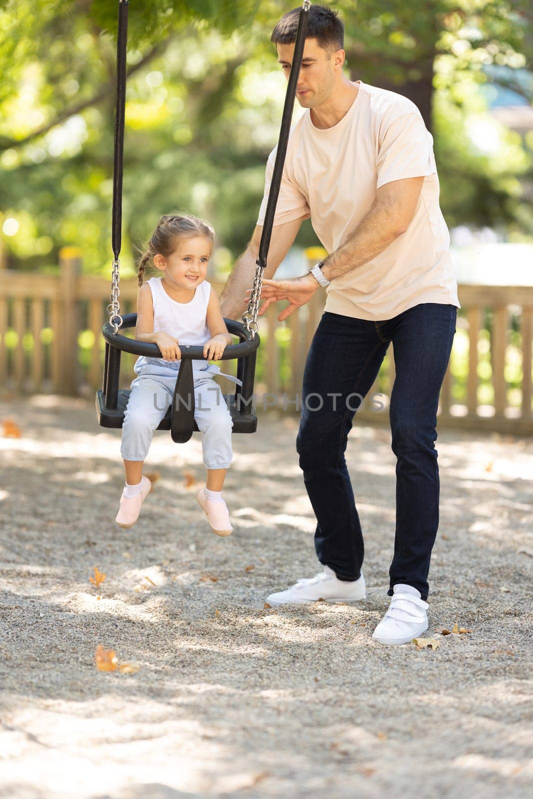 A man riding his daughter on the swings in the summer park. Mid shot