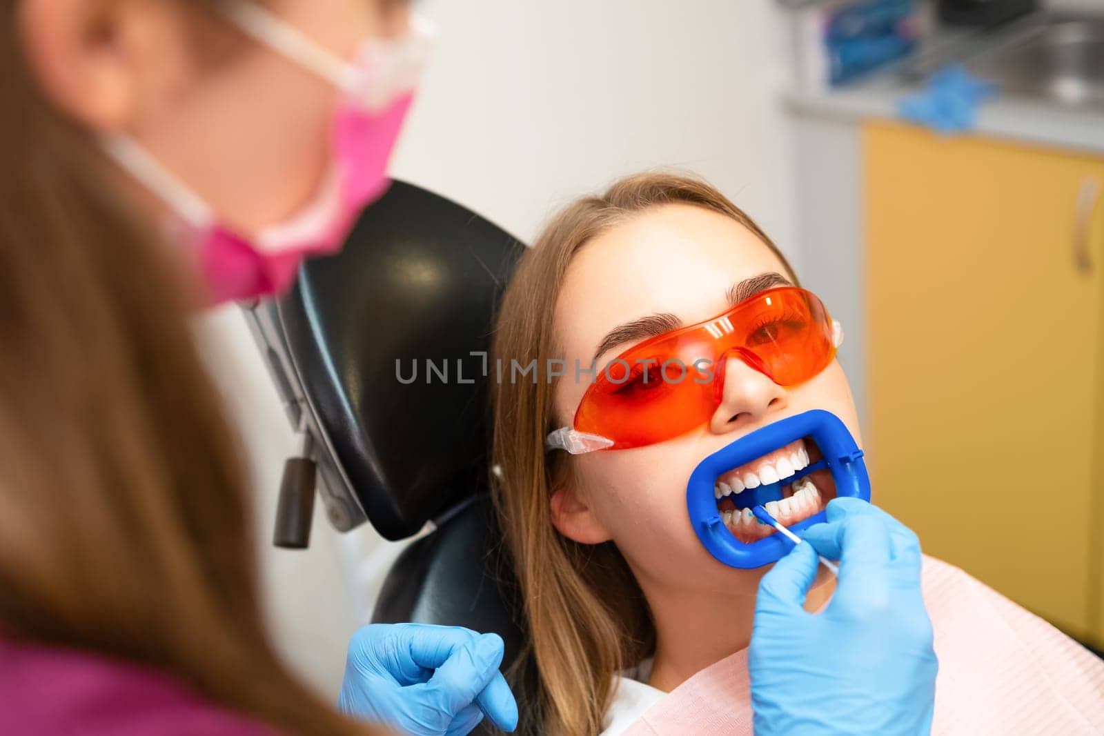 Dentist doing a whitening teeth procedure for young blond woman at the clinic by vladimka