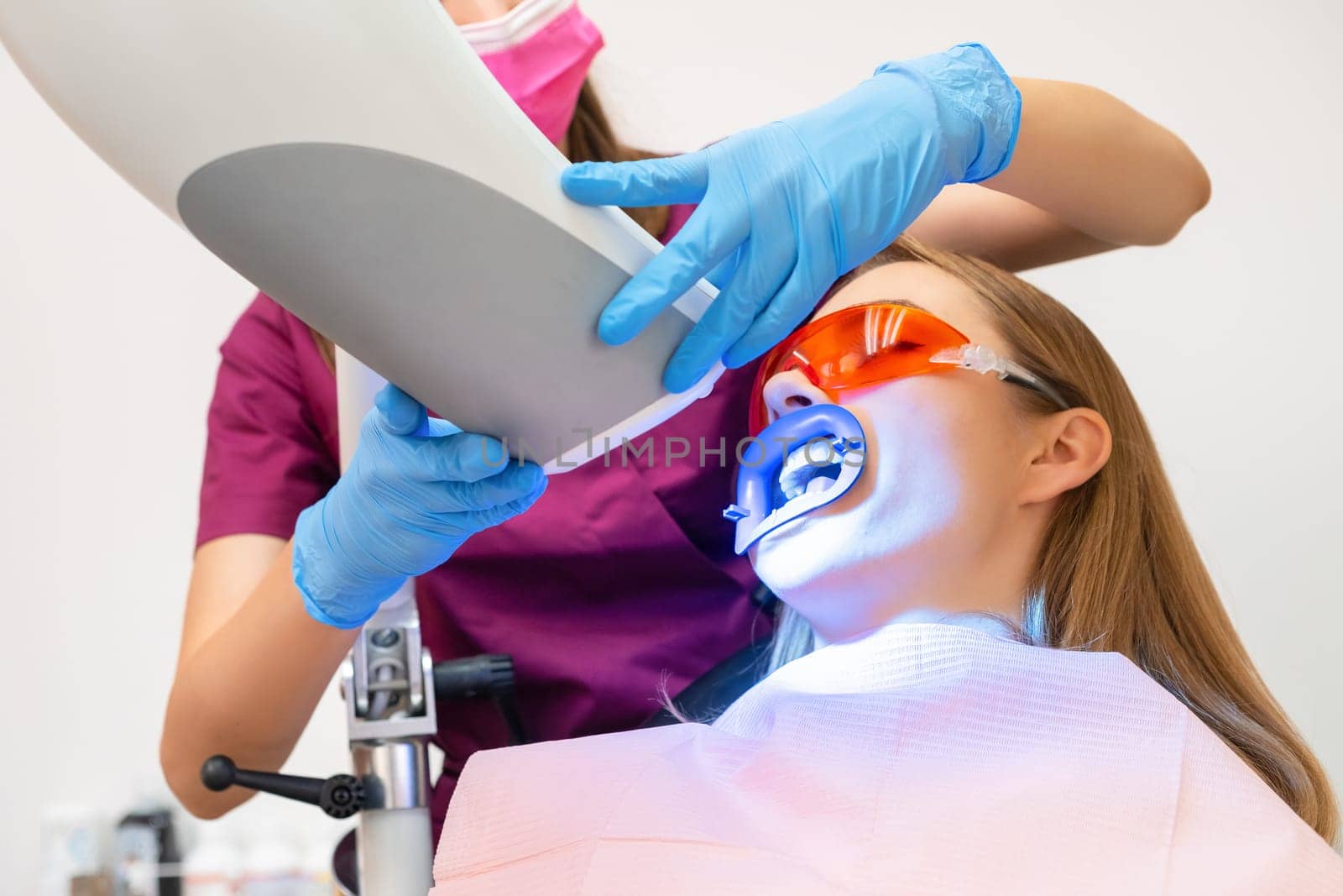 A woman undergoes teeth whitening and the application of a UV lamp for the bleaching process by vladimka